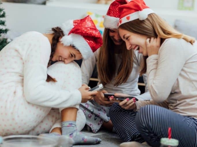 girls in pajamas and santa hats looking at their phones