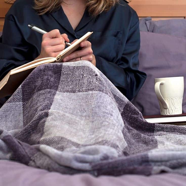 woman journaling in bed with a blanket and a cup of coffee
