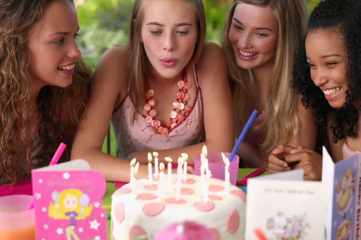 4 teenage girls, one blowing out a birthday cake's candles