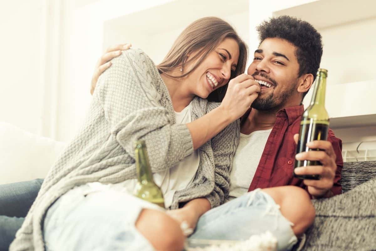 couple sitting on a couch cuddling - a man drinking a bottled drink