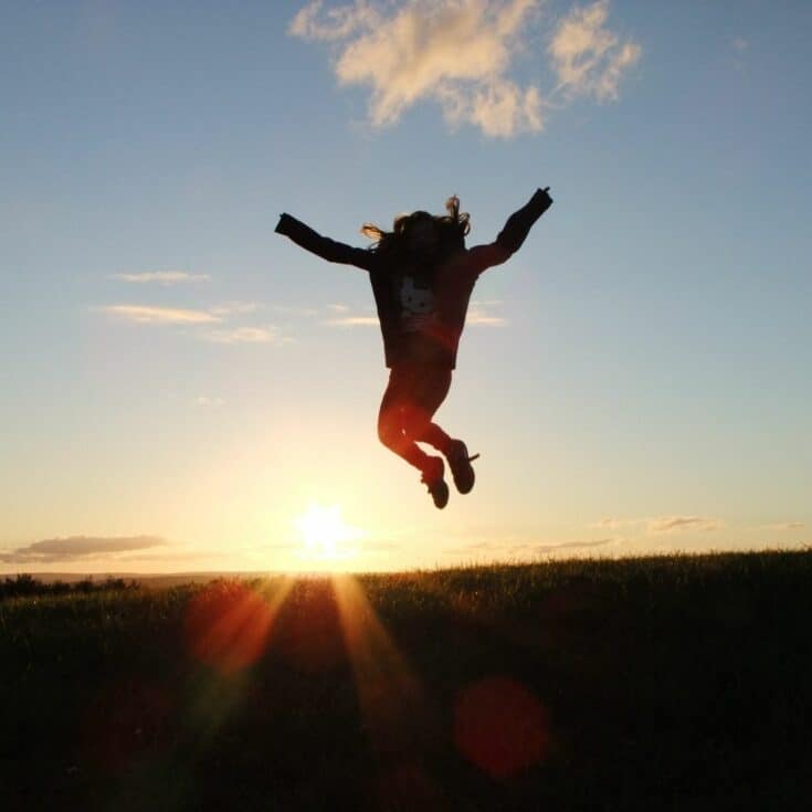 girl jumping up in the air outside against the sunlight