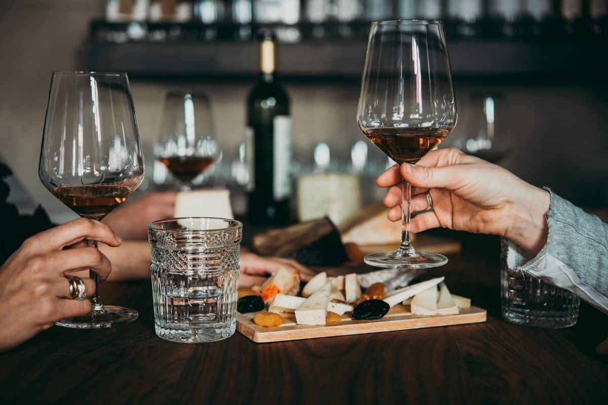 wine and cheese with 2 people's hands in the photo holding wine glasses