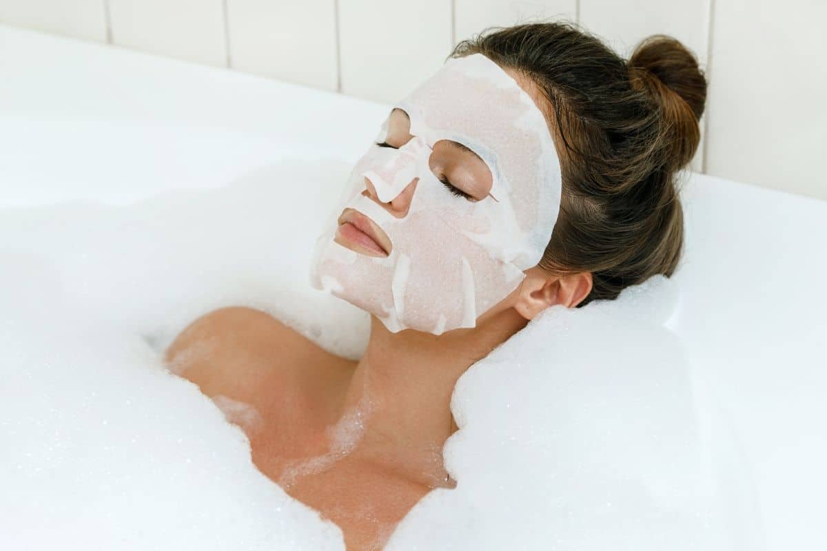 woman with a sheet mask on in the tub