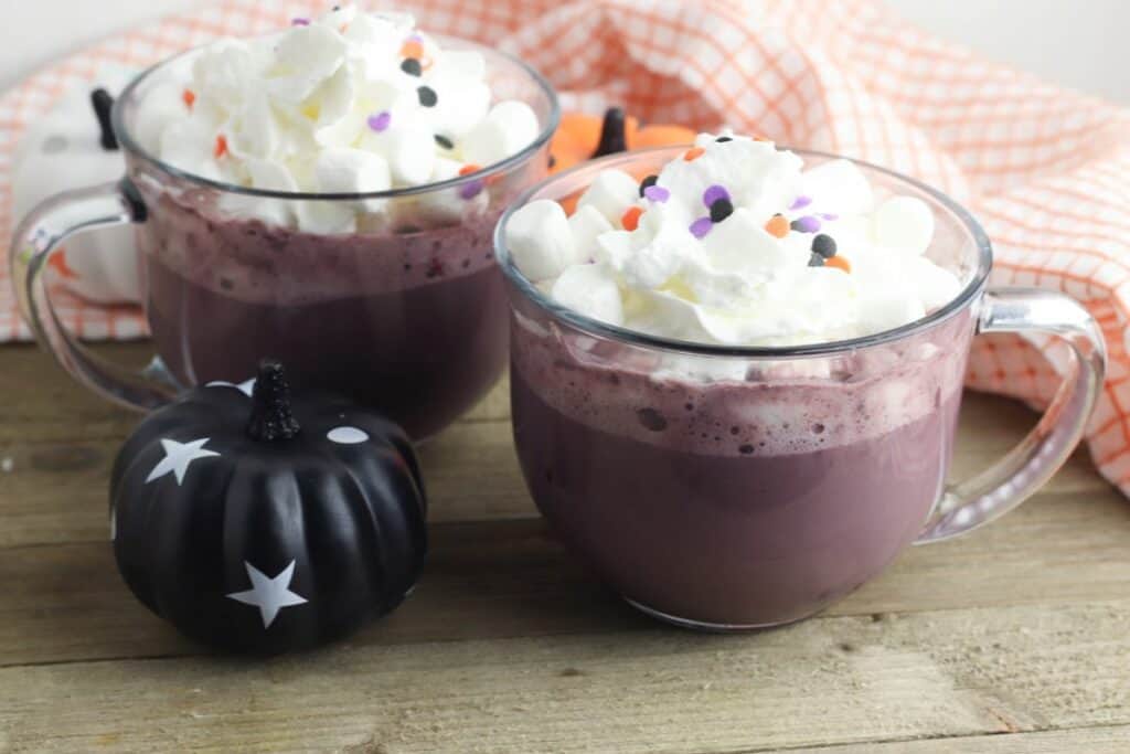 2 mugs of purple hot cocoa with halloween sprinkles