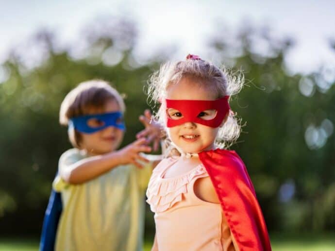 little girl with a cape and mask on - little boy in the background also wearing a cape and mask