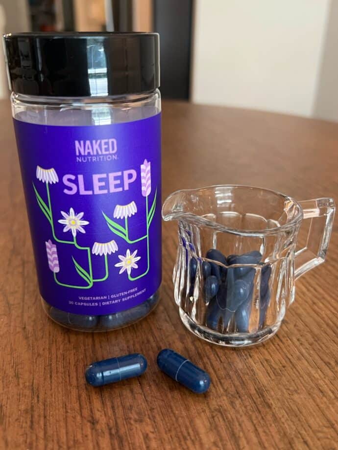 Naked Nutrition Sleep Supplement bottle and capsules in a glass container on a table