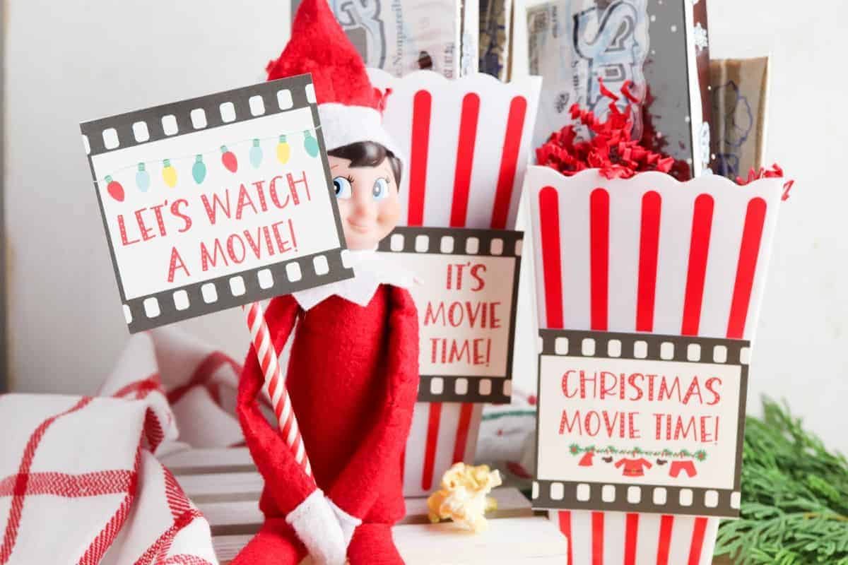 Elf on the Shelf holding a let's watch a movie sign